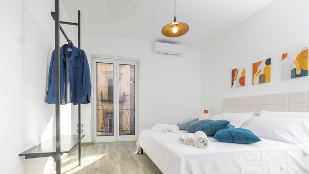 A modern bedroom with a bed, a hanging rack with clothes, a pendant light, and artwork on the wall. - Aromarìa Palace  (Palermo)