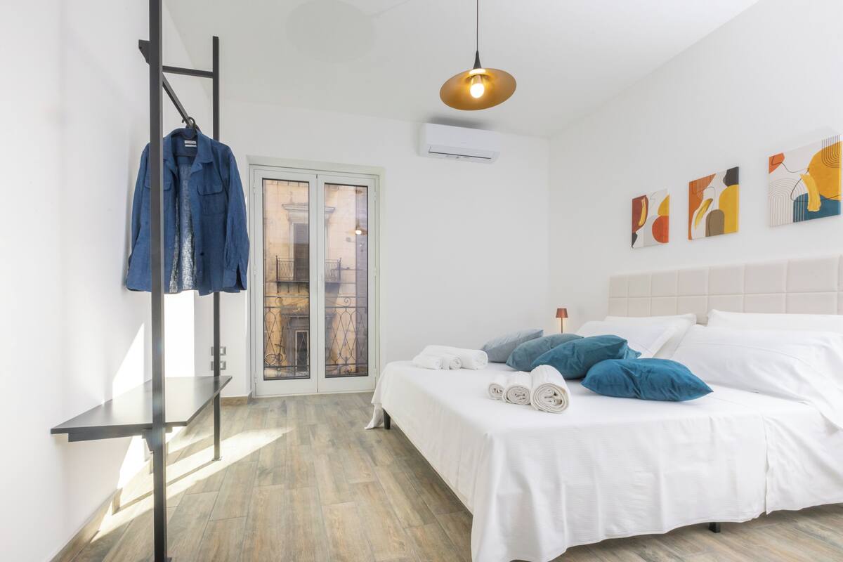 Ein modernes Schlafzimmer mit einem Bett, einem Kleiderständer, einer Pendelleuchte und einem Bild an der Wand.