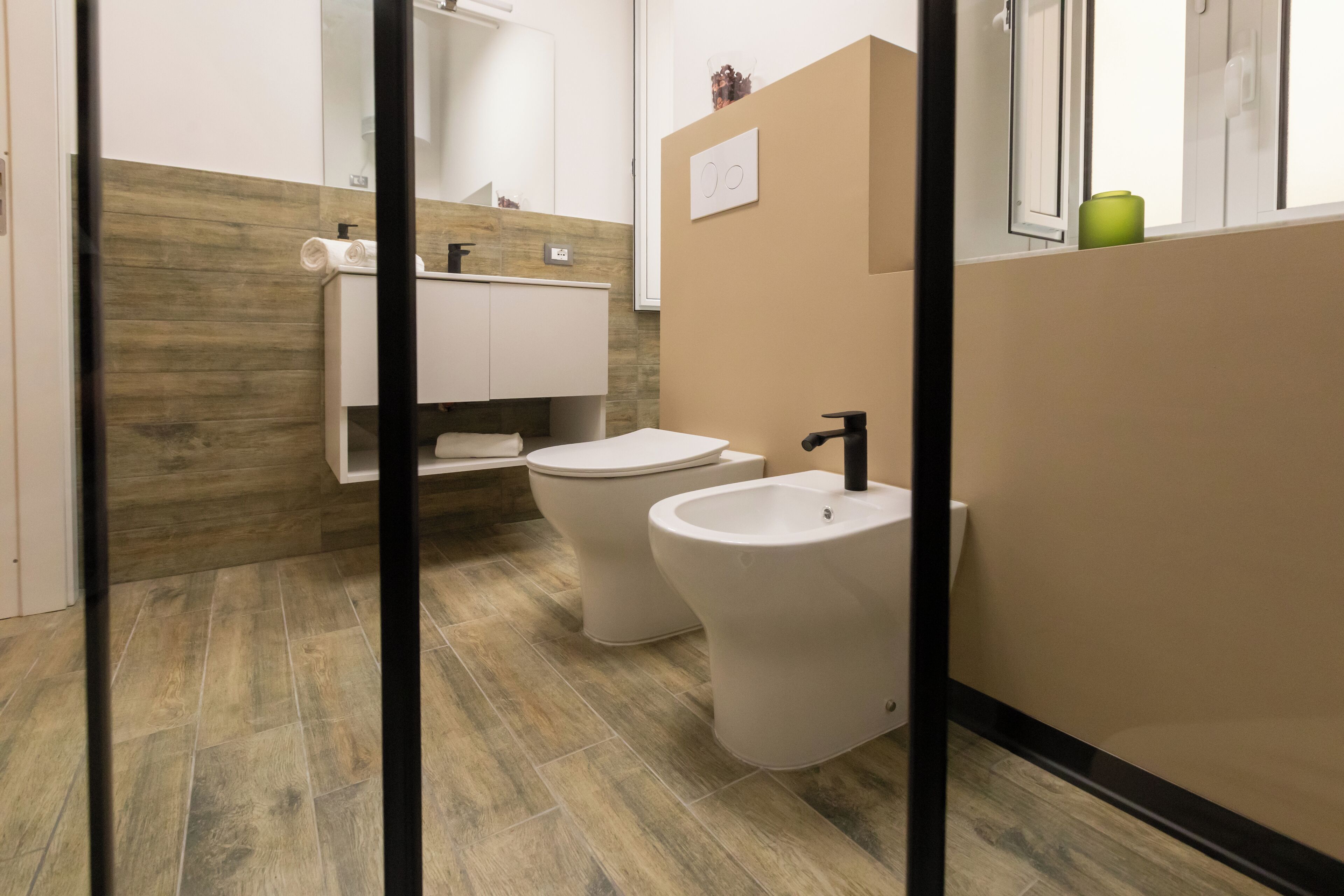 Un baño moderno con inodoro, bidé y lavabo, con suelo de madera y una paleta de colores neutros.