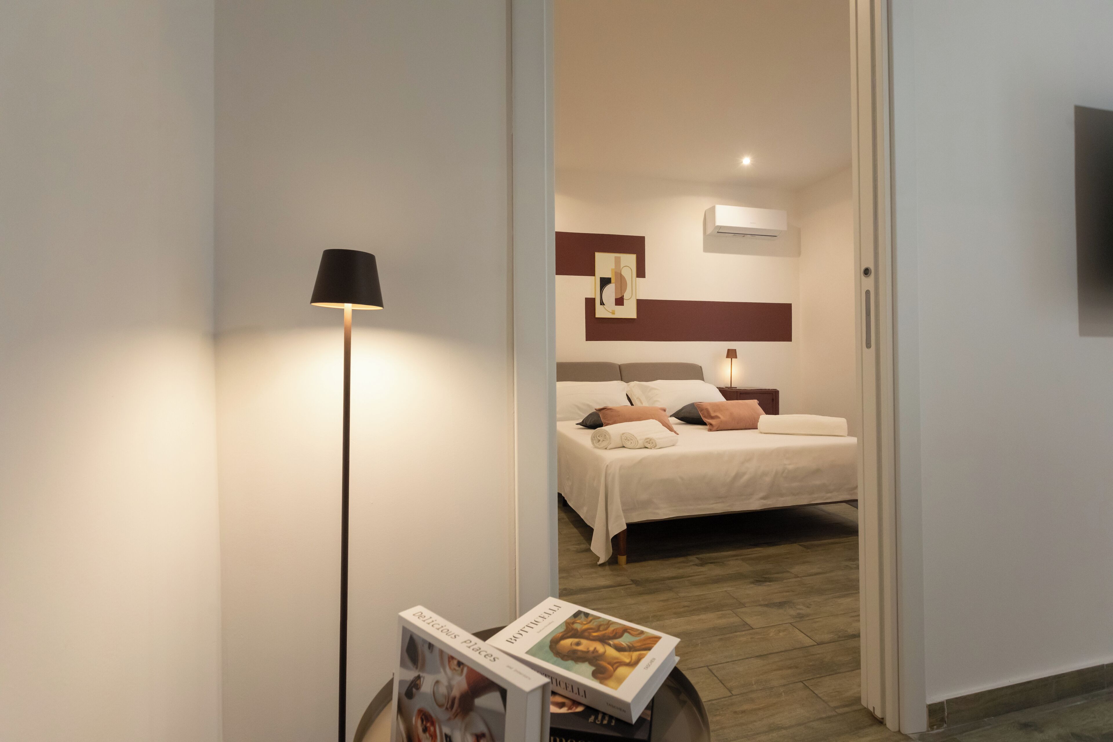 A modern hotel room with a bed, bedside table, lamp, and a magazine on the floor.