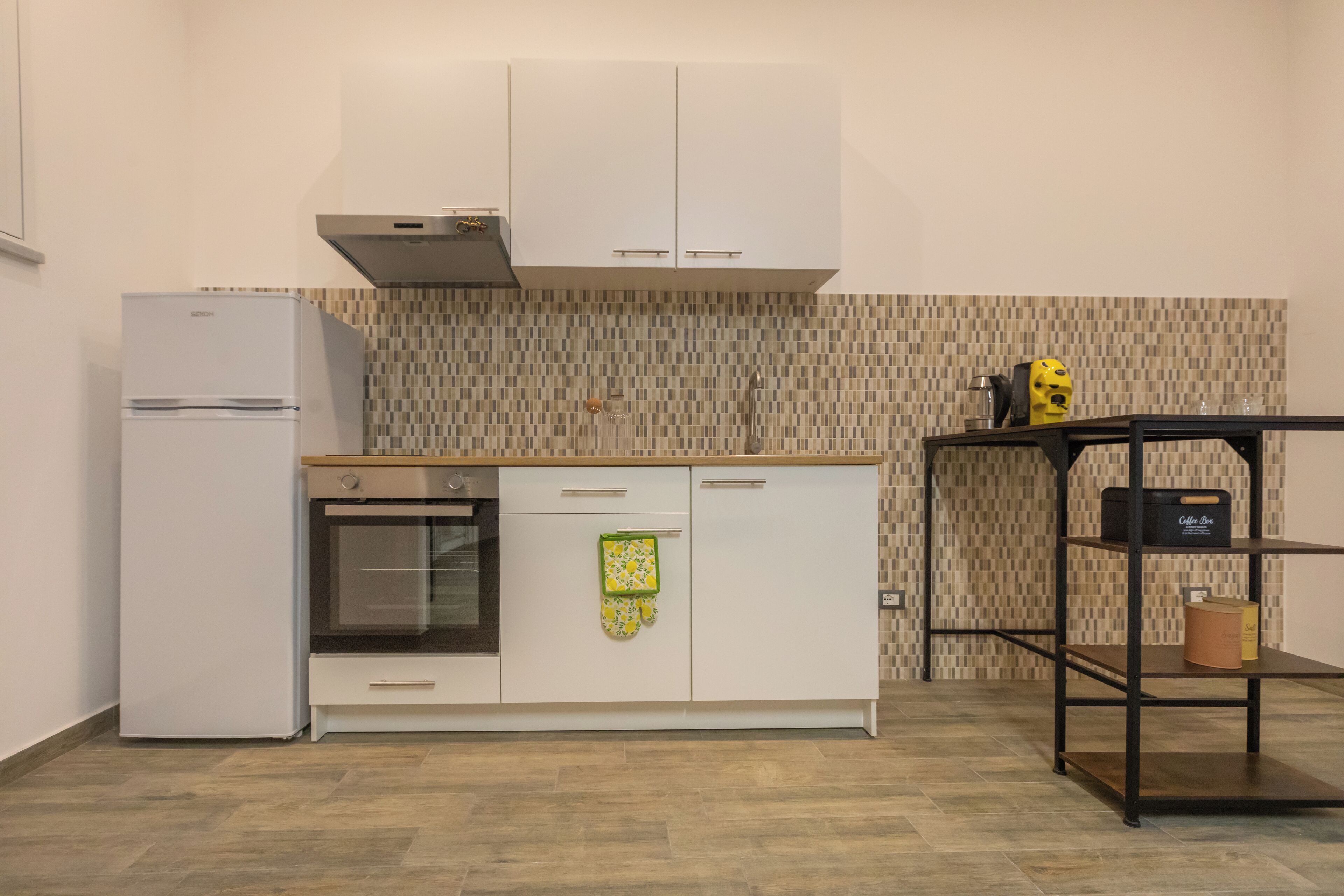Una cucina moderna con mobili bianchi, forno integrato e zoccolo a mosaico.