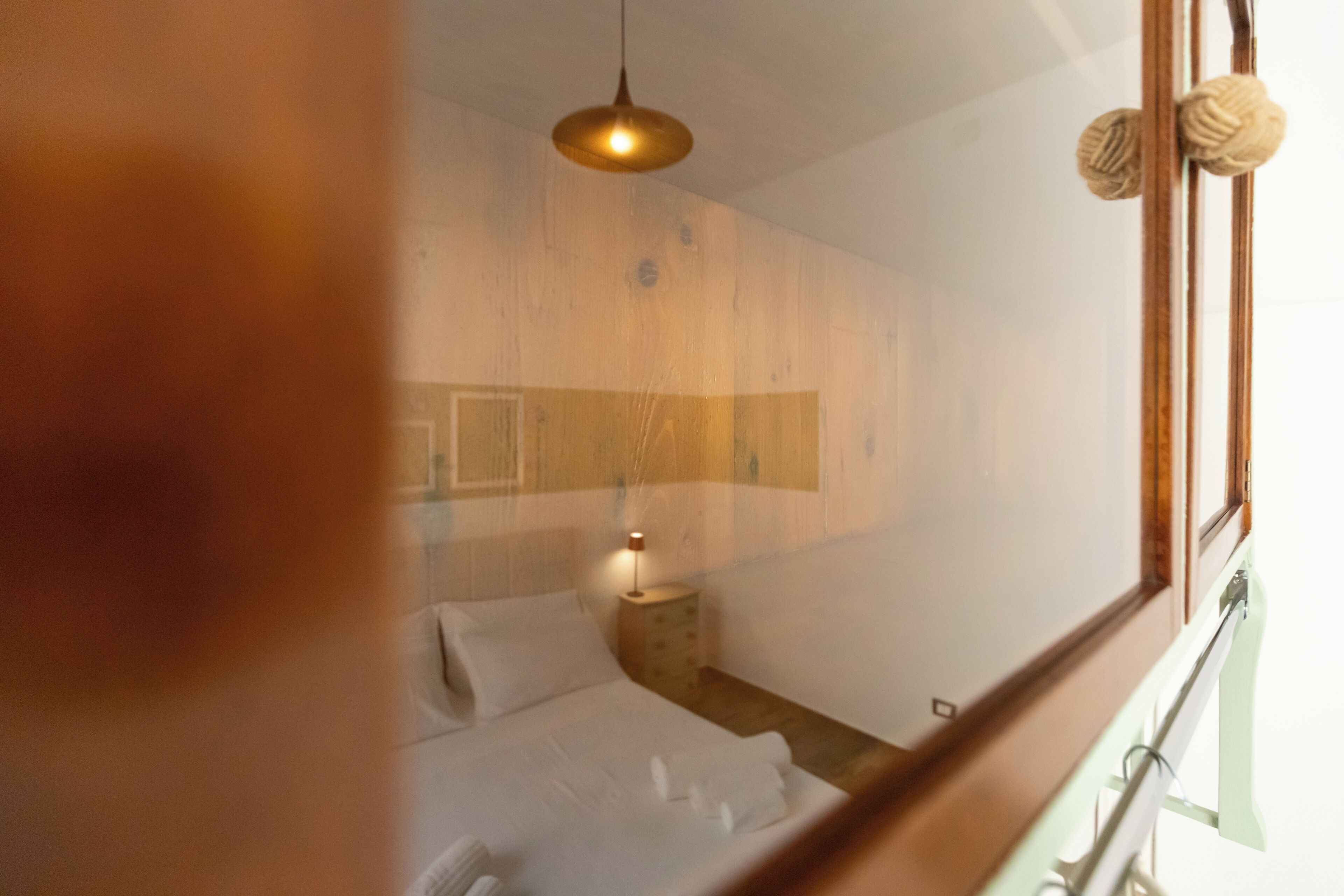 A bedroom with a bed, bedside table, lamp, and a window with a view of the outside.