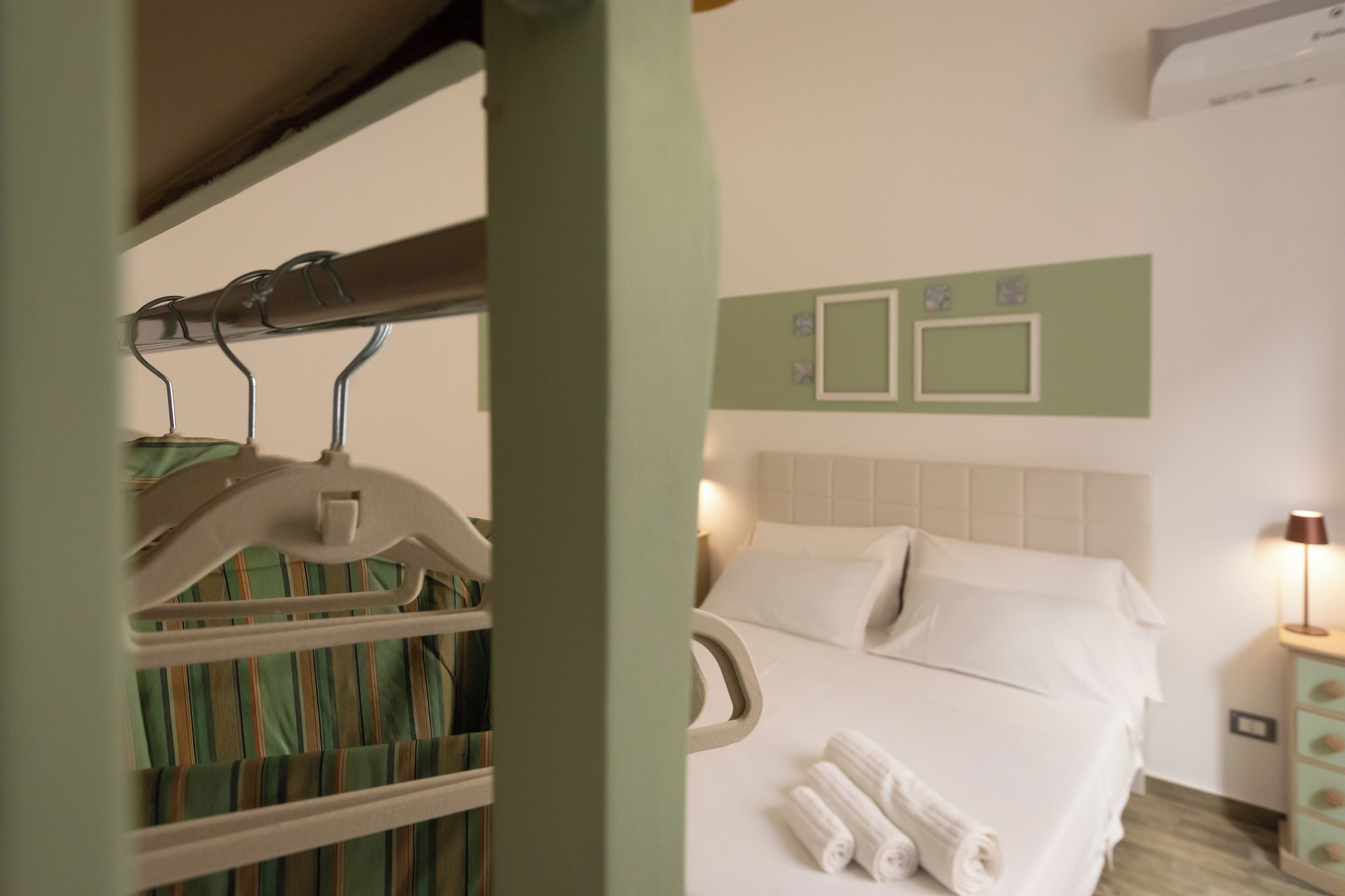 A hotel room with a bed, a nightstand, and a wall-mounted air conditioning unit.
