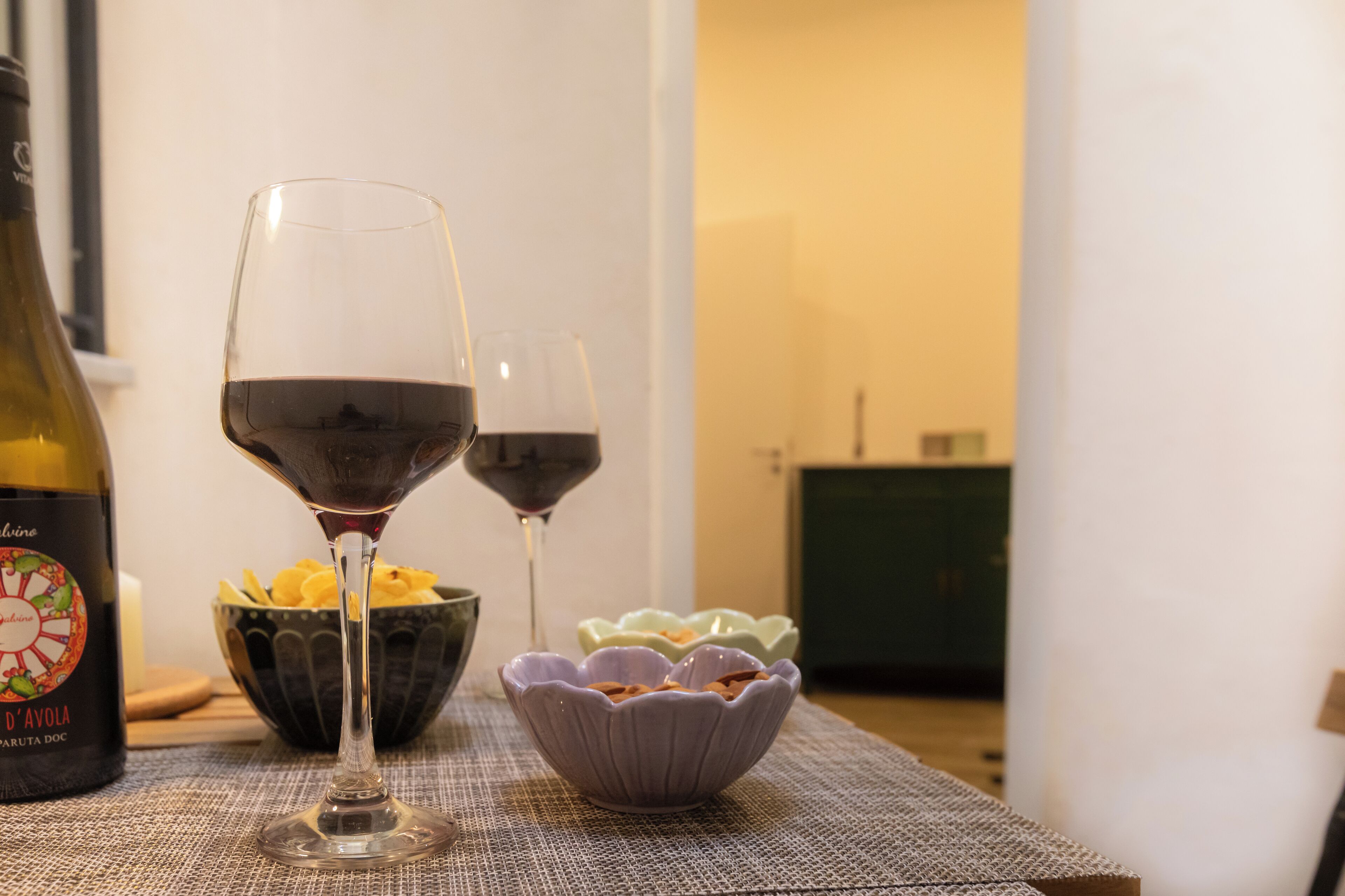 A table with two wine glasses, a bottle of wine, and bowls of snacks.