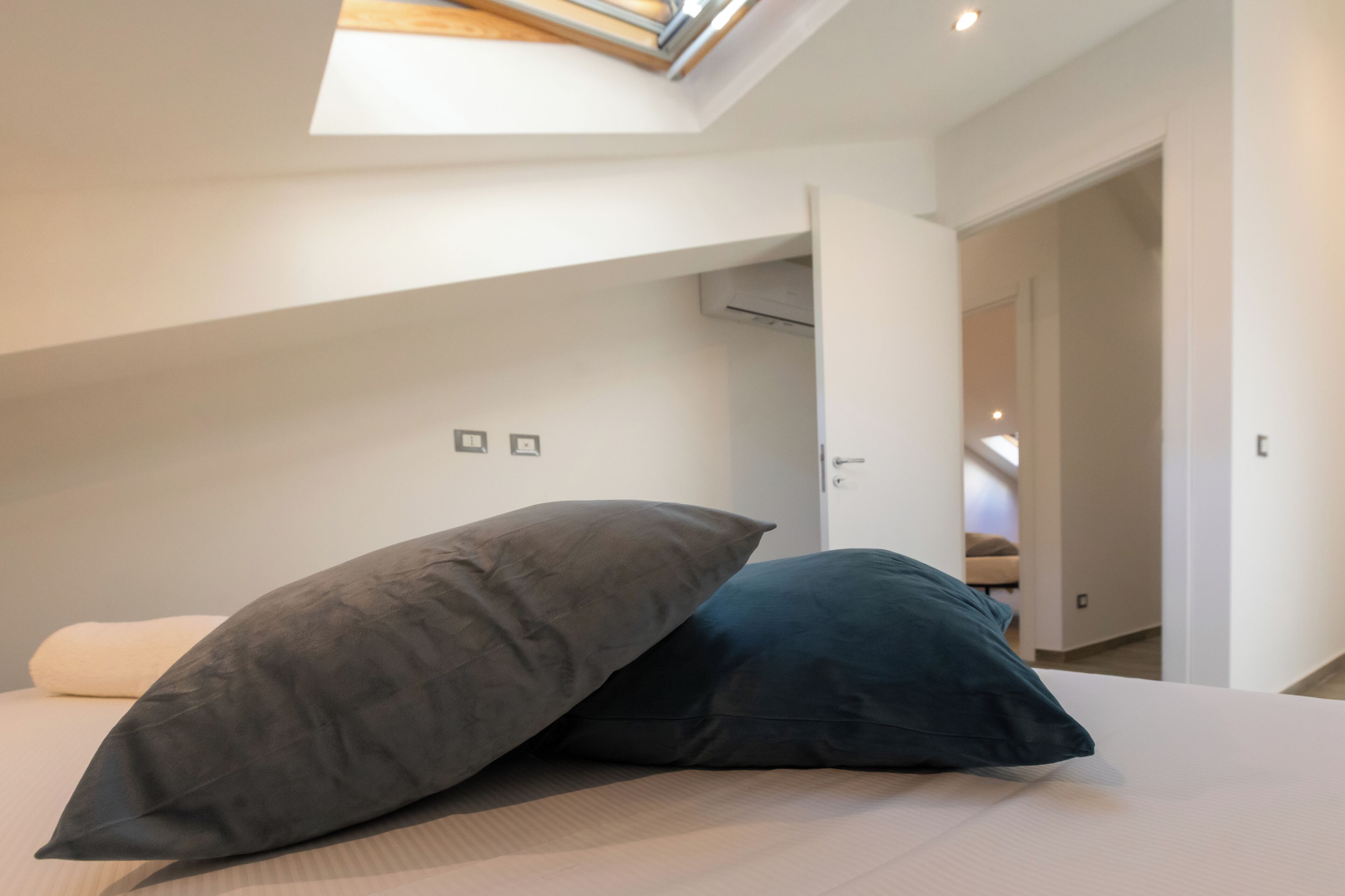 A bedroom with a skylight, a bed with two pillows, and a door leading to another room.