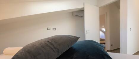 A bedroom with a skylight, a bed with two pillows, and a door leading to another room.