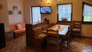 A cozy room with a wooden ceiling, a dining table with chairs, a sofa, a television, and windows with curtains. - Apartment 'Pozzobon' with Mountain View, Shared Garden and Wi-Fi (Caracoi Agoin)