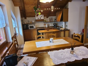 Een keuken met houten kastjes, een eettafel met stoelen, een magnetron en een spoelbak.