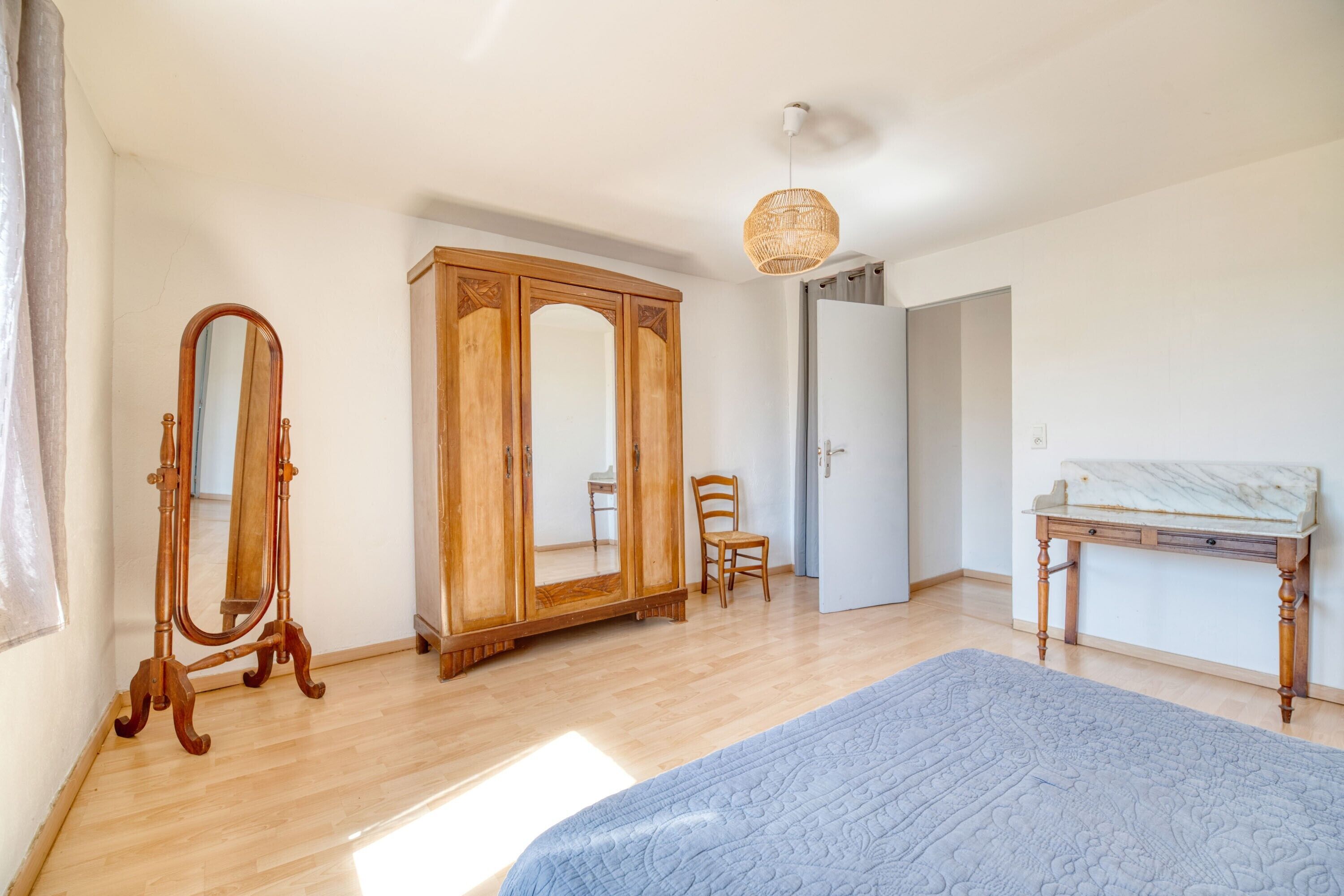 Un dormitorio con cama, armario de madera, espejo y una mesita.