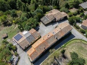 Vista aérea de una zona residencial con varios edificios, incluyendo una casa larga y estrecha con techo de tejas y una edificación más pequeña con techo inclinado.