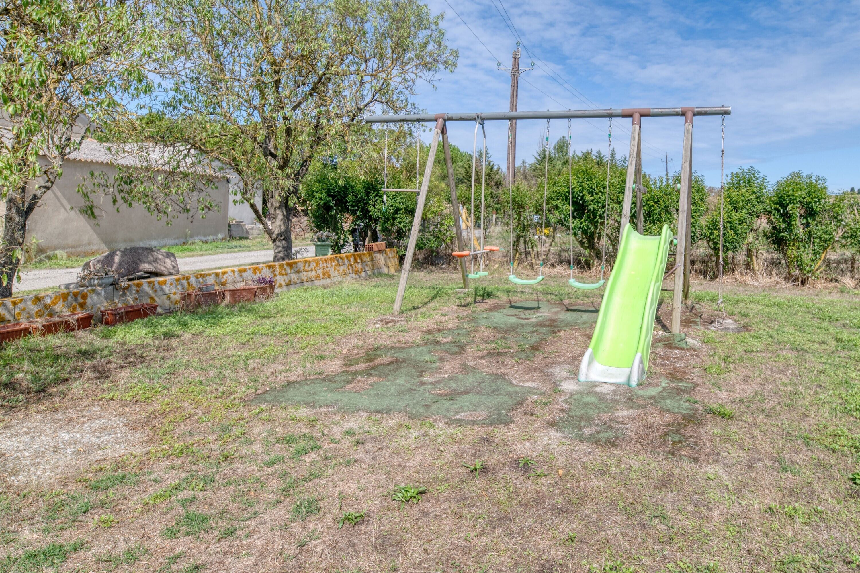 A playground with swings and a slide, surrounded by trees and a building.