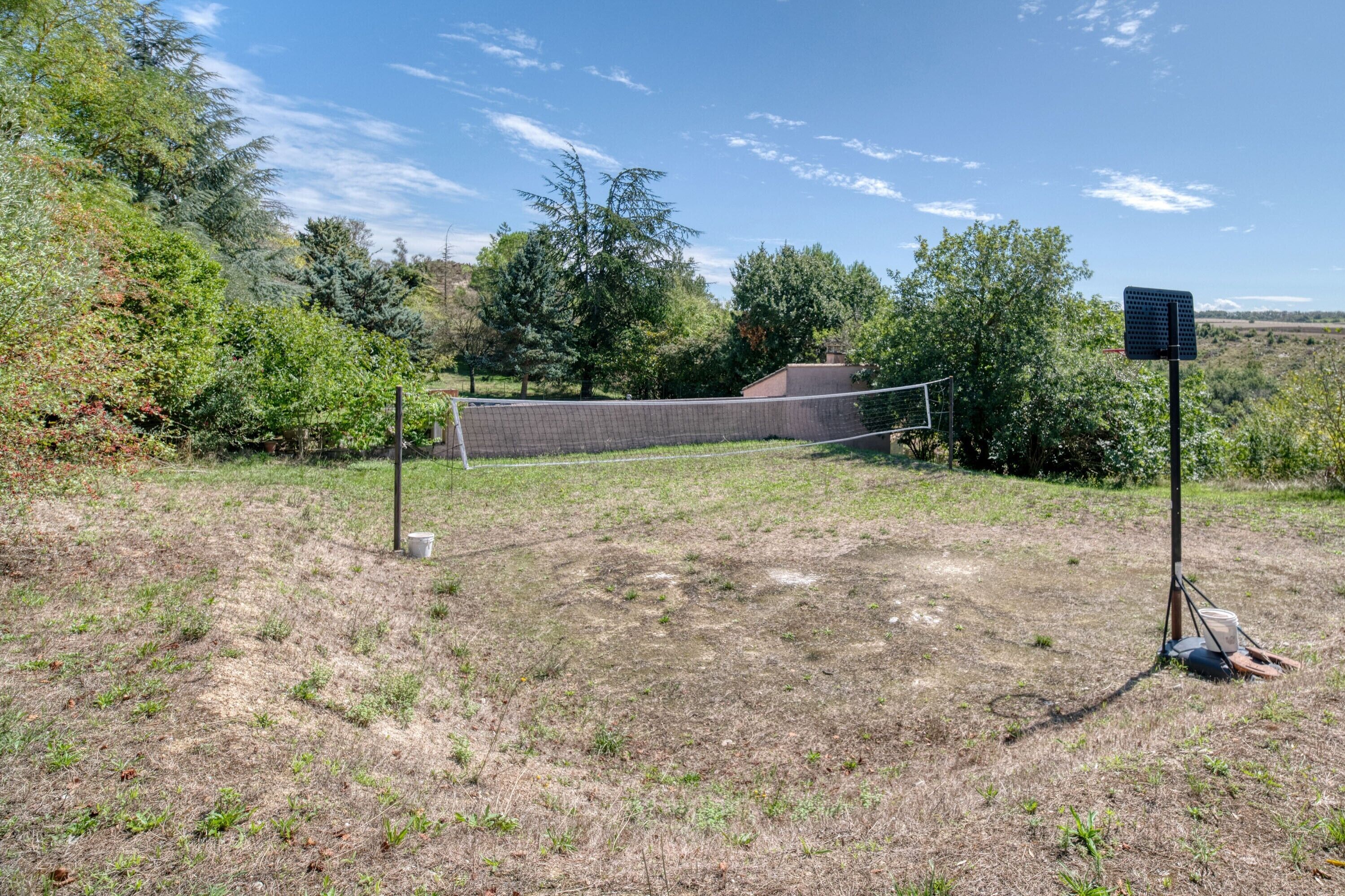 A sports field with a net, surrounded by trees and a brick wall.