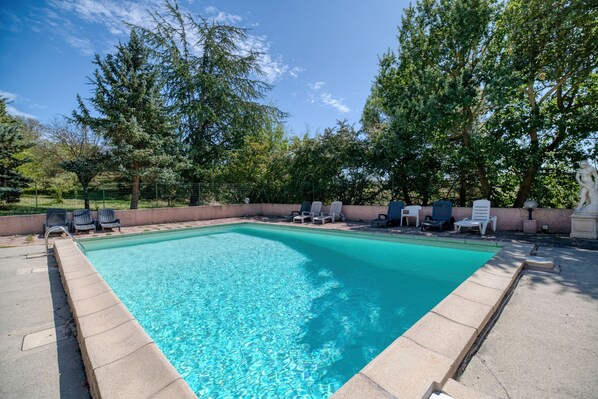 Ein rechteckiger Pool mit klarem, blauem Wasser, umgeben von einer Betonplattform und Liegestühlen.