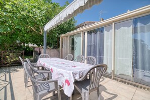 Eine Terrasse im Freien mit Tisch und Stühlen, einer Pergola und einer Glasveranda.