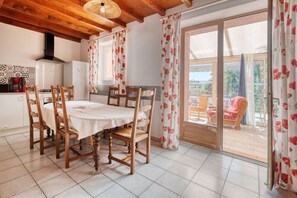 Ein Essbereich mit Tisch und Stühlen, eine Küche mit Herd und Kühlschrank sowie eine Glastür, die zu einem Außenbereich mit Sitzgelegenheit führt.