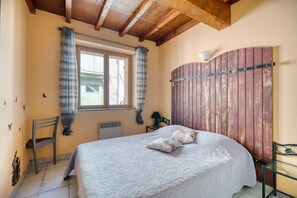 Ein Schlafzimmer mit Bett, einem Fenster mit Vorhängen, einem Heizkörper, einem Sessel und einer Holzwandverkleidung.