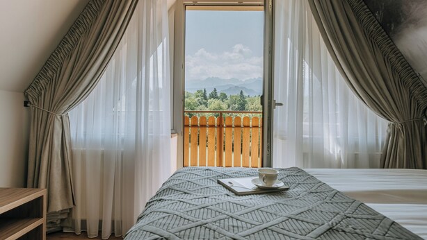 Un dormitorio con una cama, una taza en una bandeja y vistas a una valla de madera y montañas a través de un ventanal.