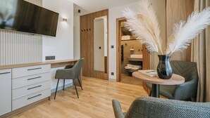 Una habitación de hotel moderna con una televisión de pantalla plana, un armario de madera, una mesa redonda con un jarrón de plumas de pampa y un sofá gris.