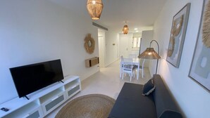 Un salon moderne avec un téléviseur à écran plat, un canapé foncé, un tapis rond et un coin repas avec des chaises blanches et une table.