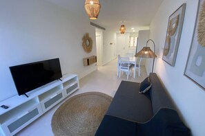 A modern living room with a flat-screen TV, a dark sofa, a round rug, and a dining area with white chairs and a table. - Playa de Puzol con terraza y piscina (Puçol)