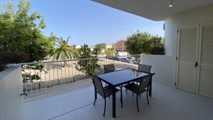 Un balcon avec une table et des chaises, donnant sur une rue bordée de palmiers et d’immeubles.