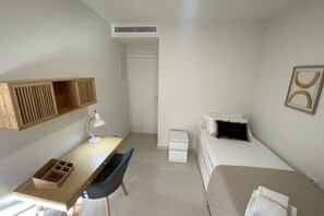 Una habitación pequeña y acogedora con un escritorio de madera, una silla, una cama, una mesita de noche y un estante en la pared.
