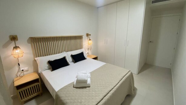 Une chambre à coucher bien rangée, avec un grand lit, des lampes de chevet, une tête de lit en bois et une armoire.
