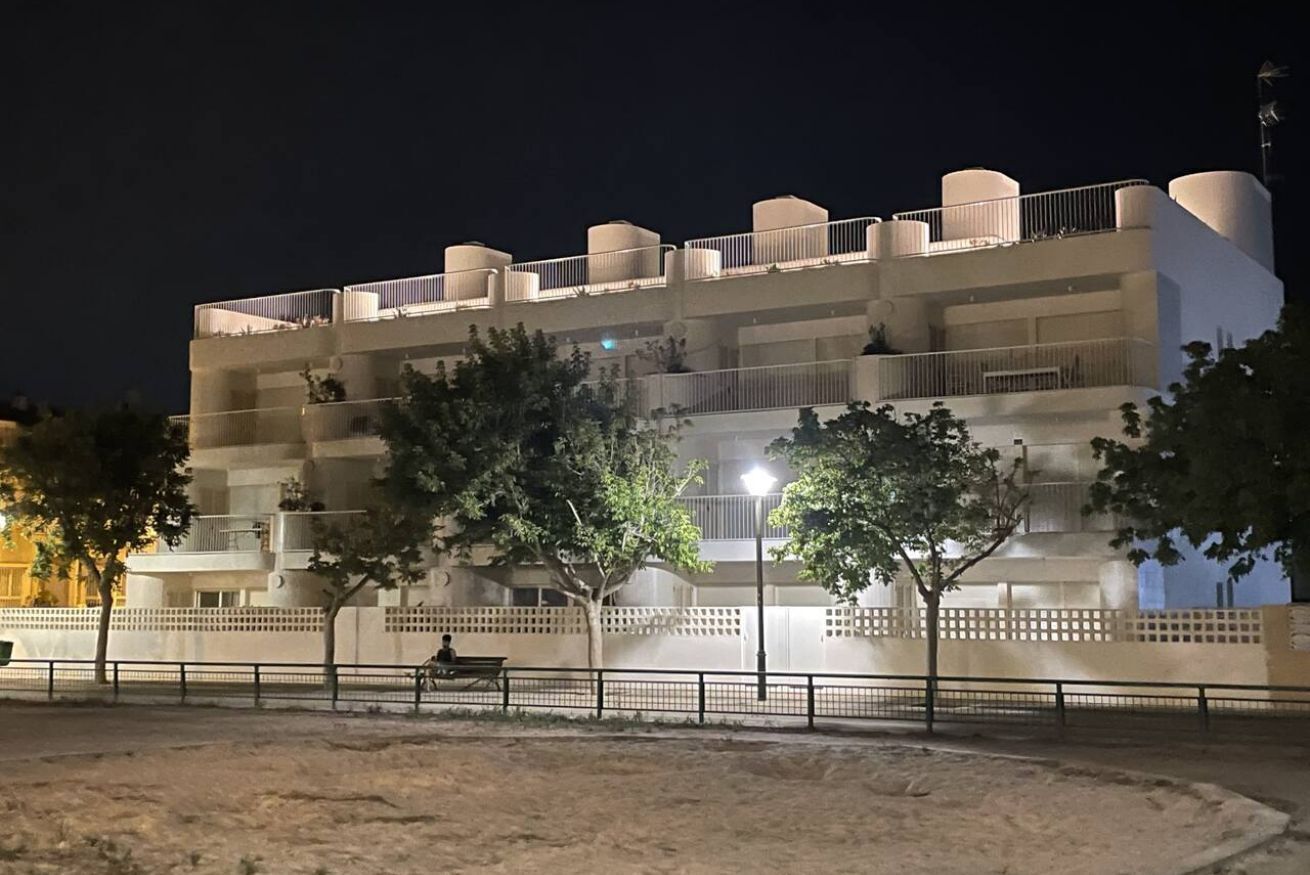 A multi-story hotel with balconies, a sandy ground floor, and trees in the foreground.