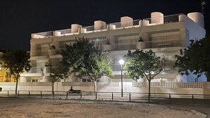 Ein mehrstöckiges Hotel mit Balkonen, einem sandigen Erdgeschoss und Bäumen im Vordergrund.