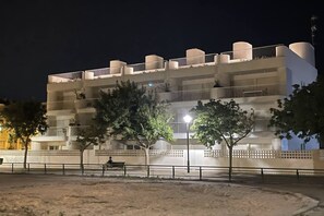 Ein mehrstöckiges Hotel mit Balkonen, einem sandigen Erdgeschoss und Bäumen im Vordergrund.
