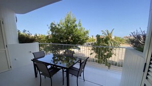Ein Balkon mit Glastisch und Stühlen, weißen Wänden und Blick auf eine Straße und Bäume.