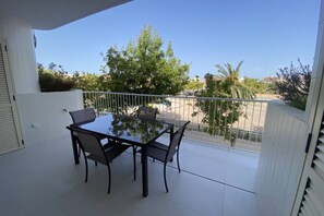 Ein Balkon mit Glastisch und Stühlen, weißen Wänden und Blick auf eine Straße und Bäume.