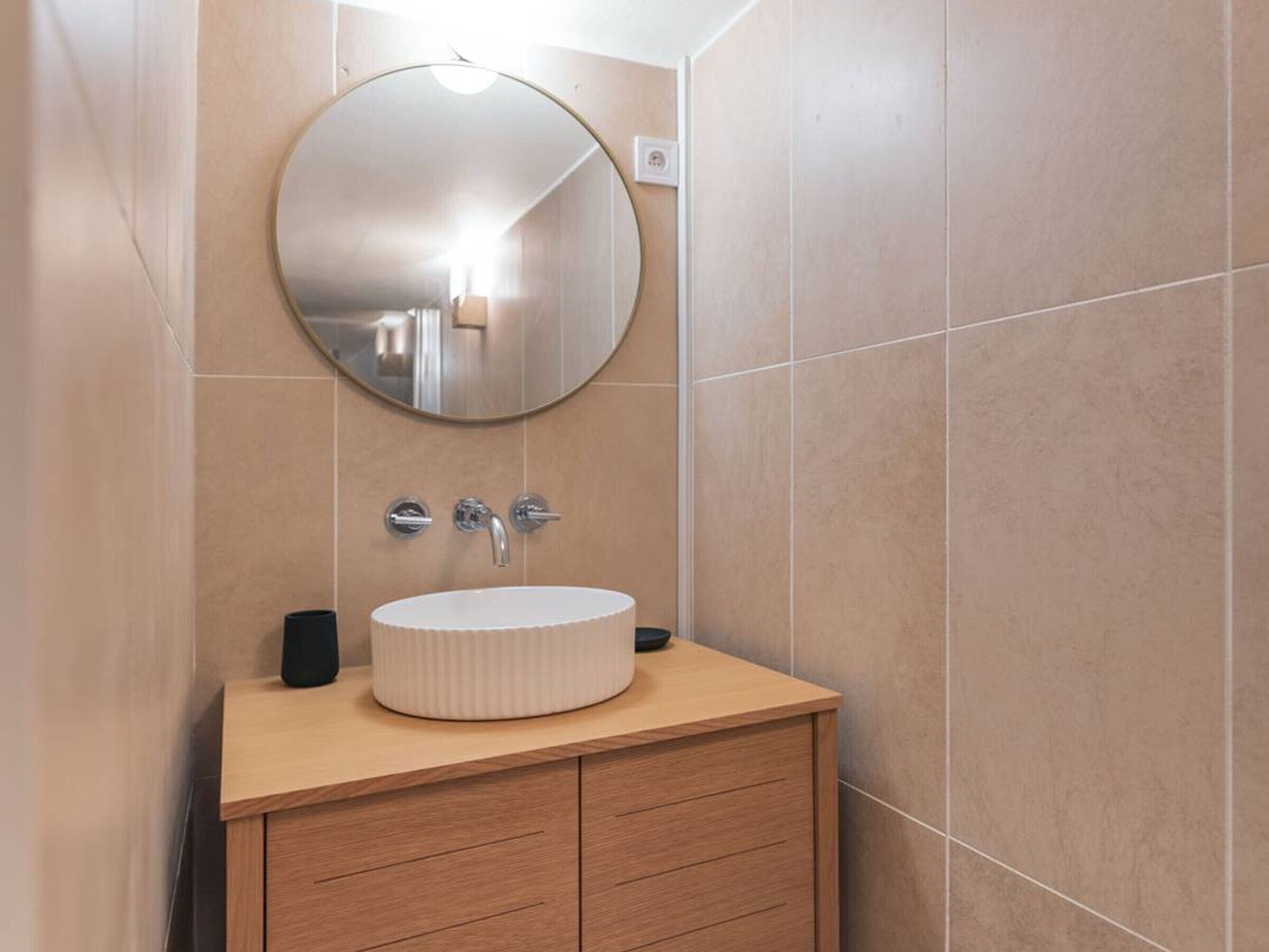 Un baño con un espejo redondo, un lavabo blanco y muebles de madera.