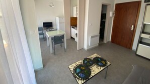 A compact living space with a dining area, kitchenette, and a small table with a decorative centerpiece. - Apartment 4 guests near beach with parking (Argelès-sur-Mer)