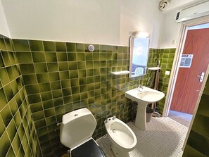 A bathroom with green tiled walls, a toilet, a bidet, and a sink.