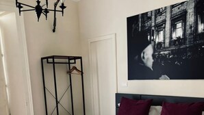 A neatly made bed with a pink quilt, two rolled towels, and a black metal rack with a wooden hanger. - Stanze di Agatha (Catania)