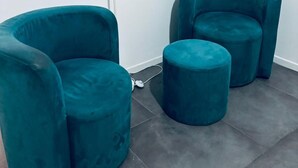 A teal-colored, curved armchair and ottoman set against a white wall, with a white floor lamp beside them. - Stanze di Agatha (Catania)