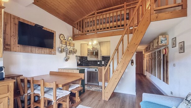A wooden staircase leading to an upper level, a dining area with a table and chairs, a kitchen with modern appliances, and a living area with a sofa. - 2-room duplex with balcony and Wifi facing Mont Blanc (Combloux)