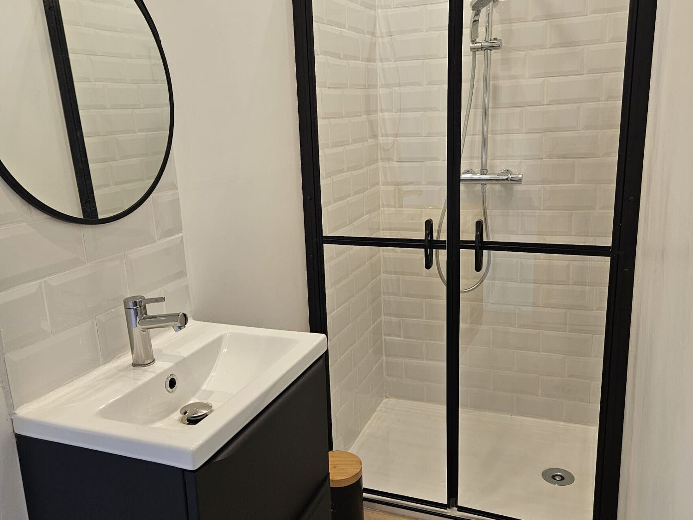 A modern bathroom with a white sink, black cabinets, a glass shower enclosure, and a mirror on the wall.