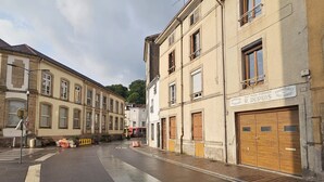 Une rue bordée d’immeubles, un panneau indiquant la limitation de vitesse et un panneau publicitaire pour le magasin de meubles R. Dupuis.