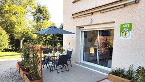 Une terrasse avec une table et des chaises, une clôture en bois et un panneau indiquant qu’il s’agit d’un gîte.