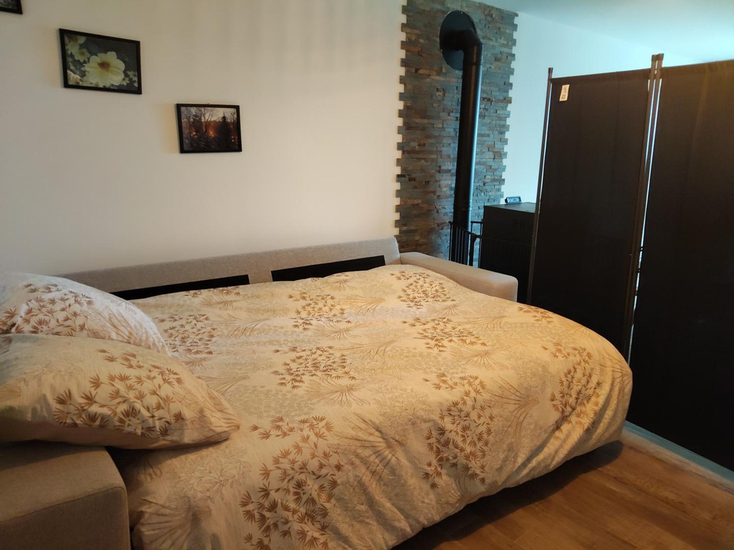 Un dormitorio con cama, suelo de madera, pared de ladrillo y armario negro.