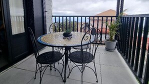 A balcony with a round table and four chairs, a potted plant, and a view of the sea.