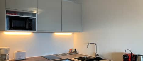 A compact kitchen with a microwave, toaster, sink, and coffee maker.