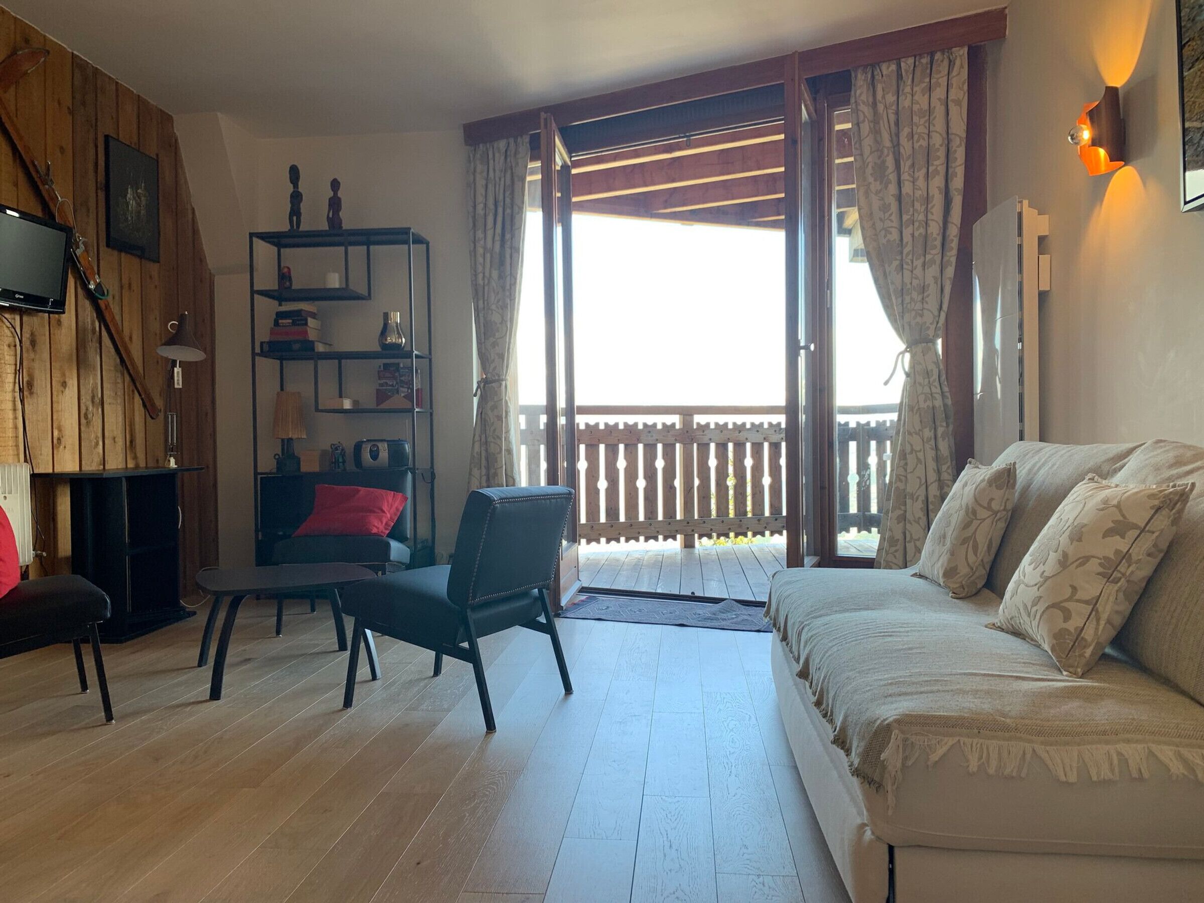 Een gezellige woonkamer met een houten vloer, een bank, een fauteuil, een boekenkast en een televisie.