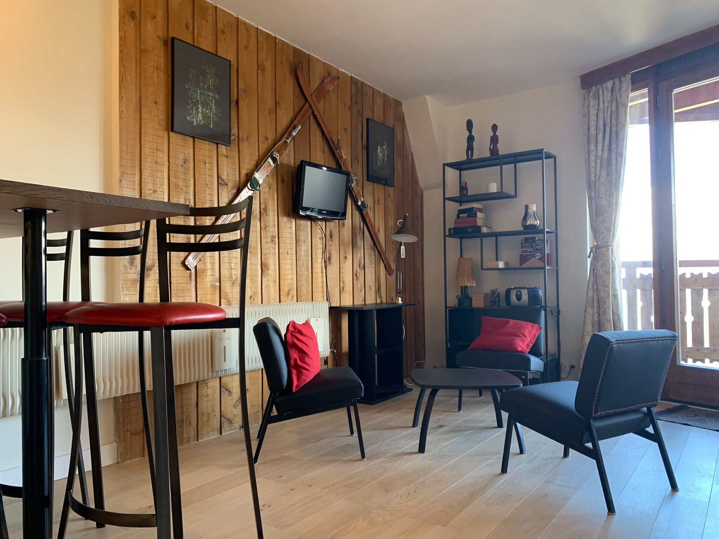 A cozy living room with wooden walls, a fireplace, and a TV mounted on the wall. There are two chairs and a small table in the room.