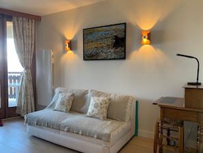 A living room with a sofa, two wall-mounted lamps, a painting, and a wooden side table.