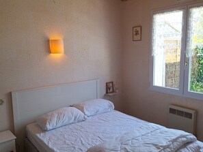 Une chambre à coucher comprenant un lit, une table de chevet, une lampe fixée au mur, une fenêtre avec vue et un radiateur.