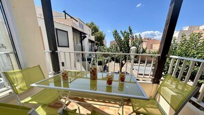 Ein Balkon mit einem Glastisch und gelben Stühlen, mit Blick auf ein Wohngebiet mit Bäumen und Gebäuden.