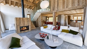 Amplia sala de estar con chimenea, sofás blancos y comedor con sillas rojas.
